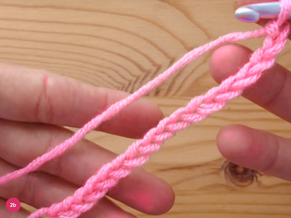 A loose pink crochet chain stretched across the fingers with the hook at the top edge