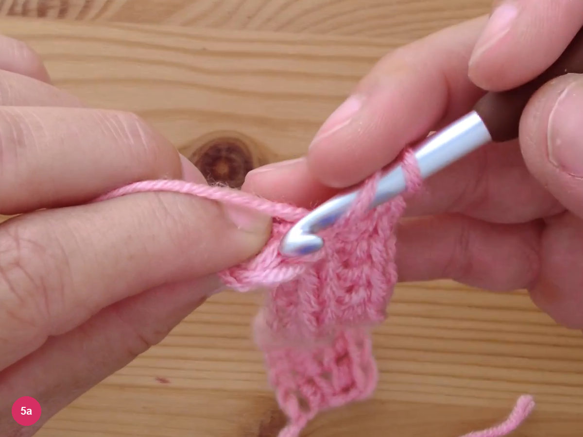 The hook working the last stitches at the edge of a row with a narrow ribbed strip hanging below