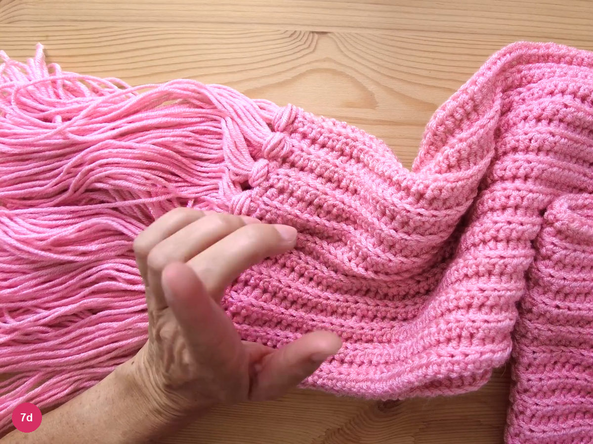 The end of the scarf with a thick row of pink fringe hanging beside the ribbed fabric