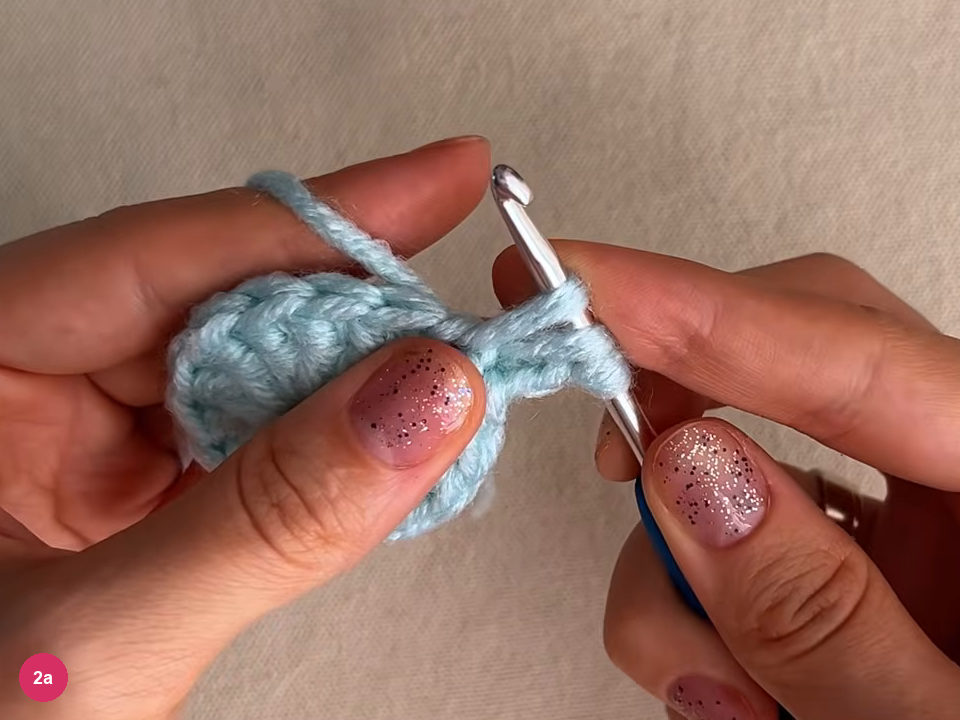 Hook at the edge of the small mint round as round 2 begins, with the outer row of stitches visible