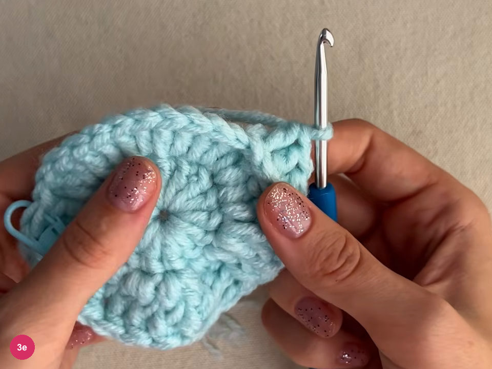 Mint round held in both hands, the hook upright at the right edge and a small stitch marker visible at the left edge