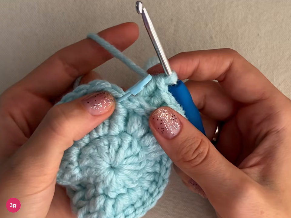 Flat mint round with a blue stitch marker clipped at the upper left of the work and the hook at the round's edge