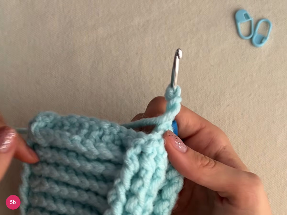 Hook standing above the turned edge of ribbed fabric, with rows of raised stitches beside and below it