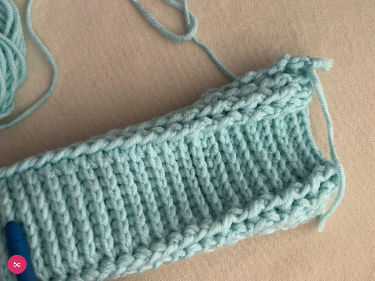 Flat ribbed mint heel section laid on the cloth with a yarn tail at the top and the hook handle at the lower left