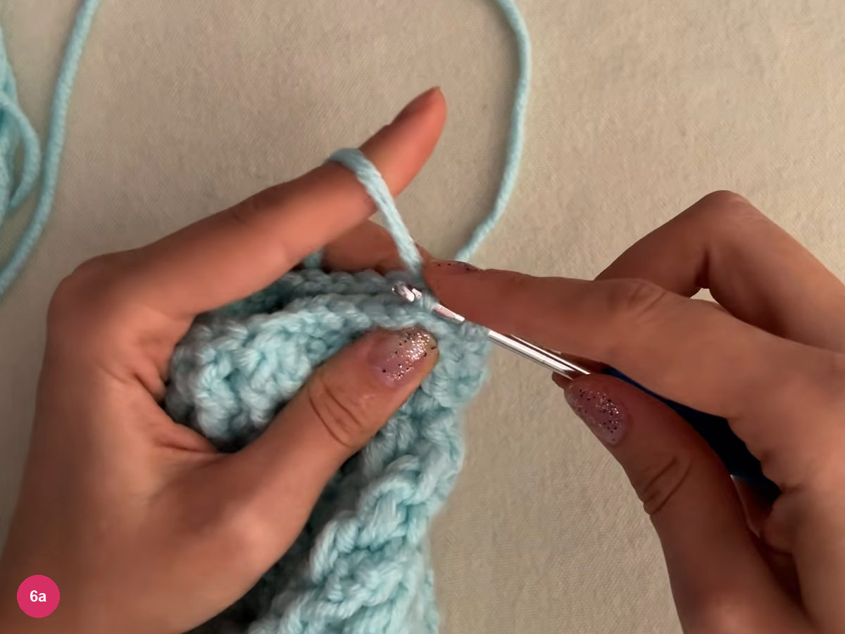 Hook inserted at the folded edge of the ribbed piece, yarn held over the left finger