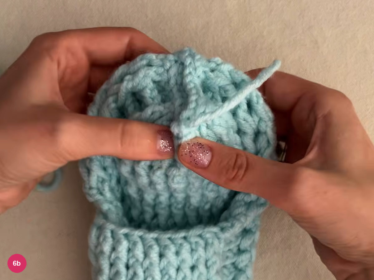 Rounded closed heel of the ribbed mint slipper held by both hands, with a yarn end lying across the seam