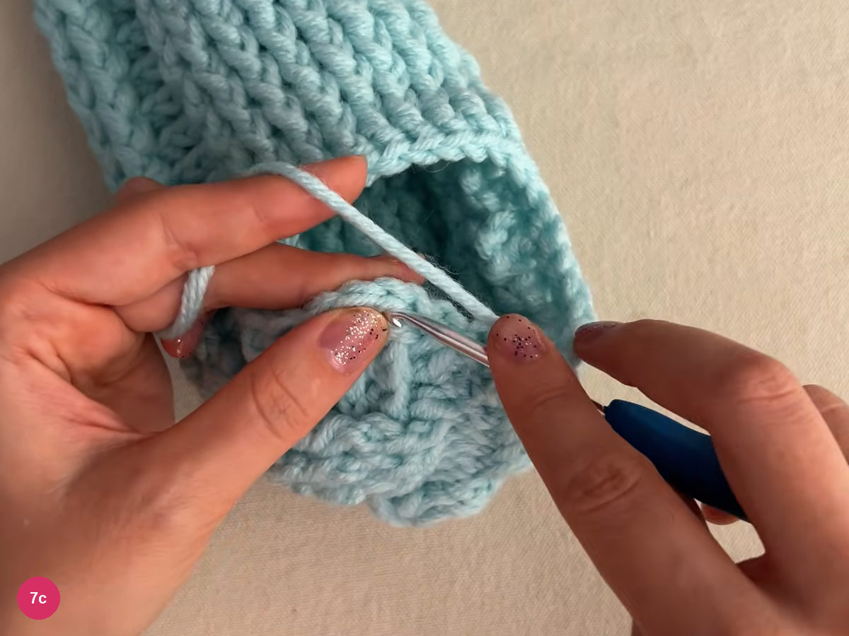 Hook working into the edge of the heel opening with yarn crossing over it and the ribbed side above