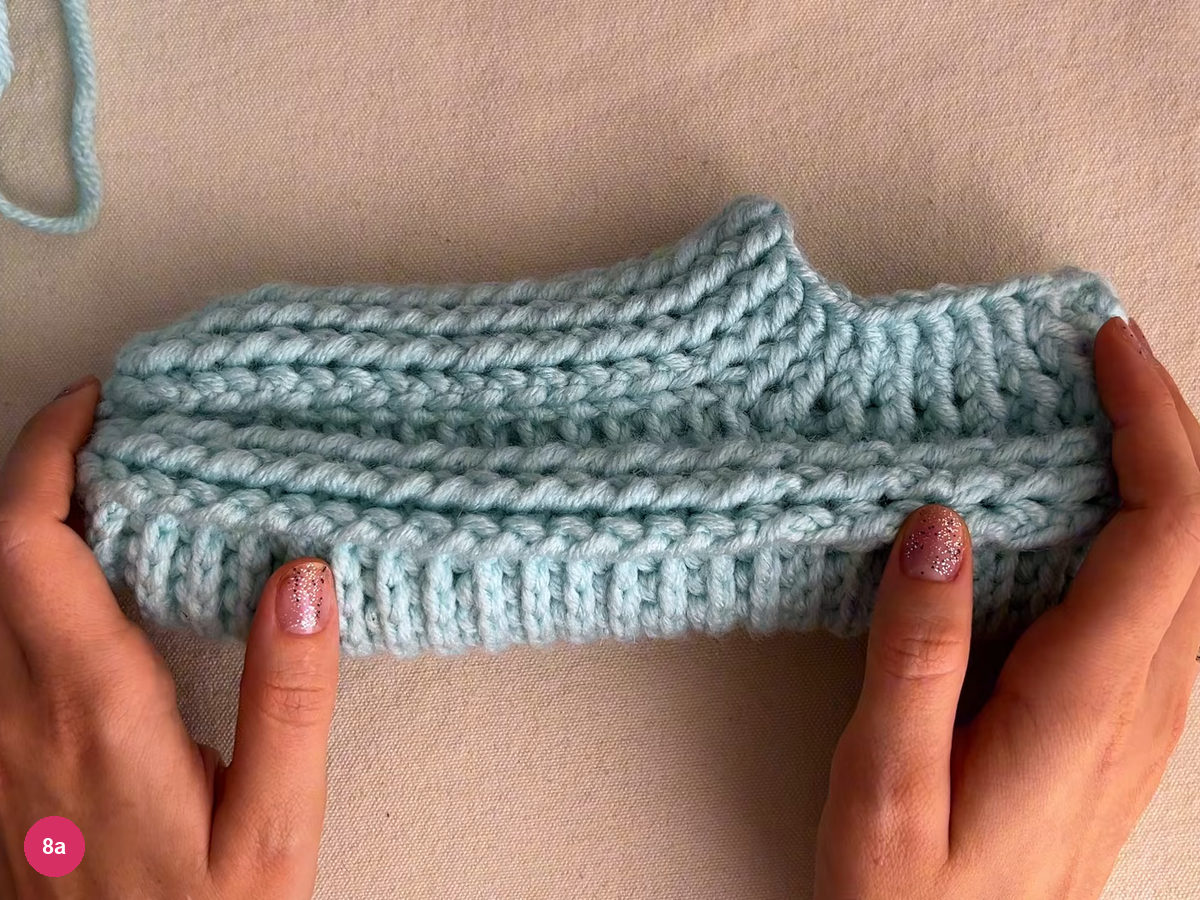 Finished mint slipper seen from the side with ribs along the body and a raised collar at one end, held by two hands