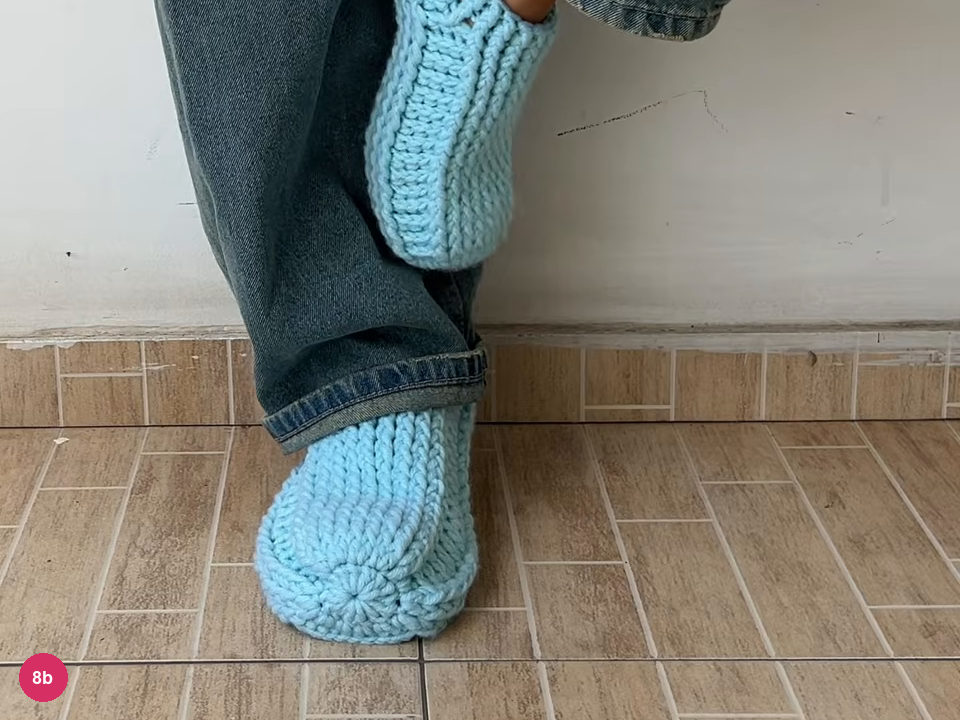 One mint slipper on a foot standing on tiles with the other foot raised, showing the round toe and the ribbed side