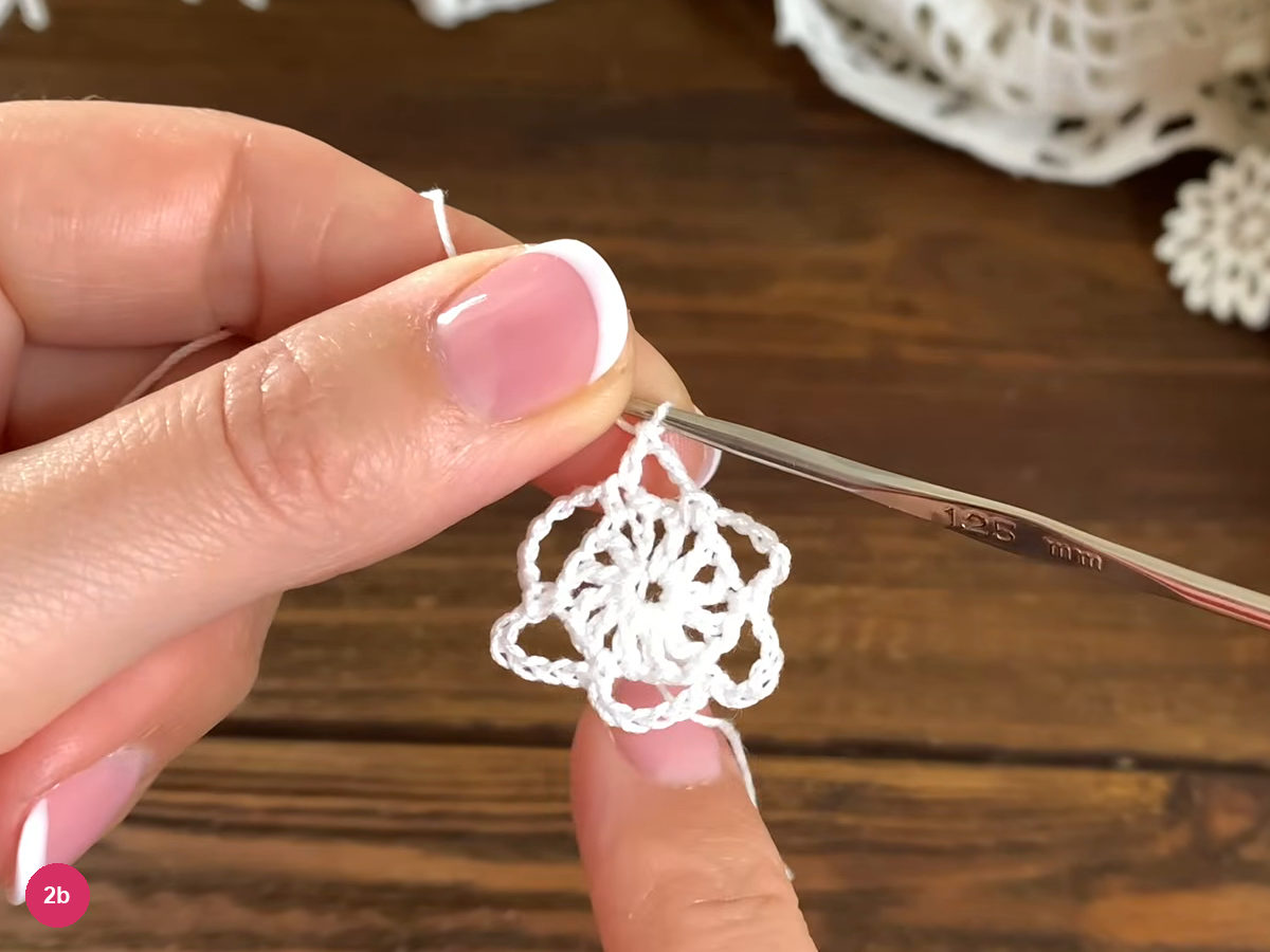 Round two opened toward the camera, showing its chain arches beneath the hook after the closing double crochet