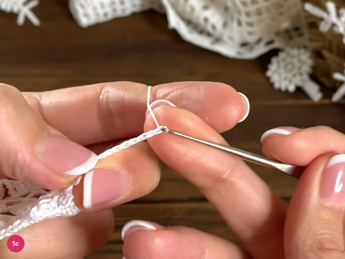 White chain strand held between the fingers and hook while forming a long picot