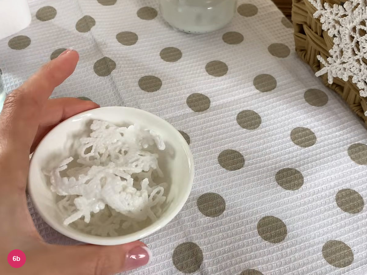 White lace rests in glue mixture inside a shallow bowl held above the work surface