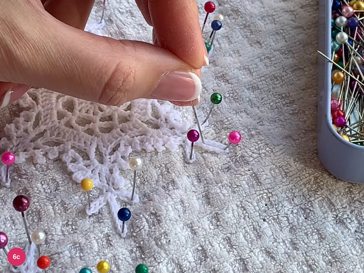 Pins hold the long lace loops open against a white towel while a hand adjusts a point
