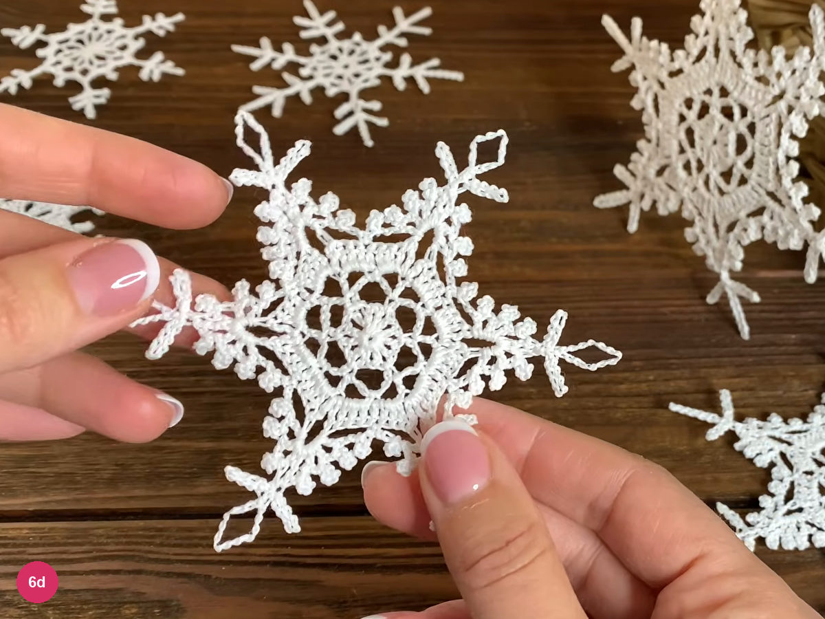 Dry six-point white lace snowflake held against a dark wood background