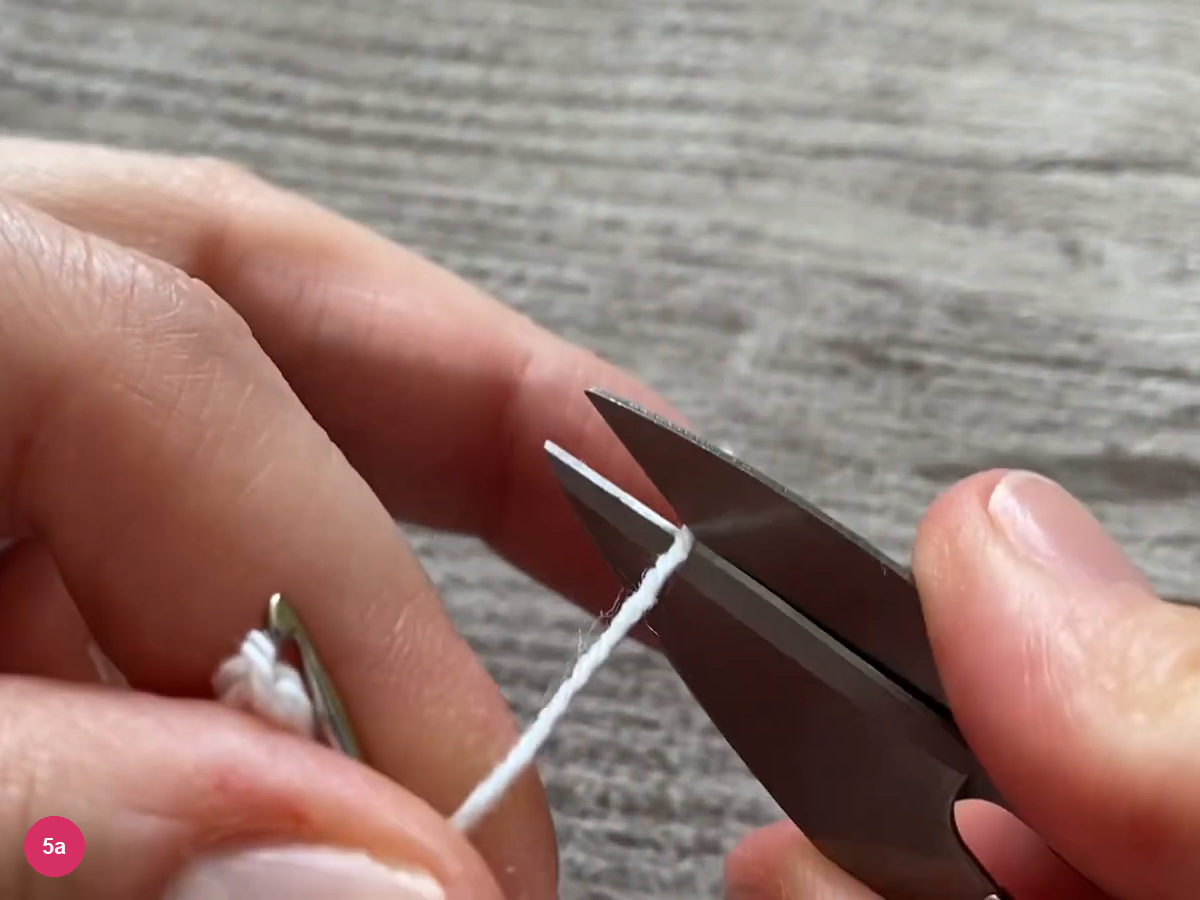 Scissors cutting the white yarn beside the hook